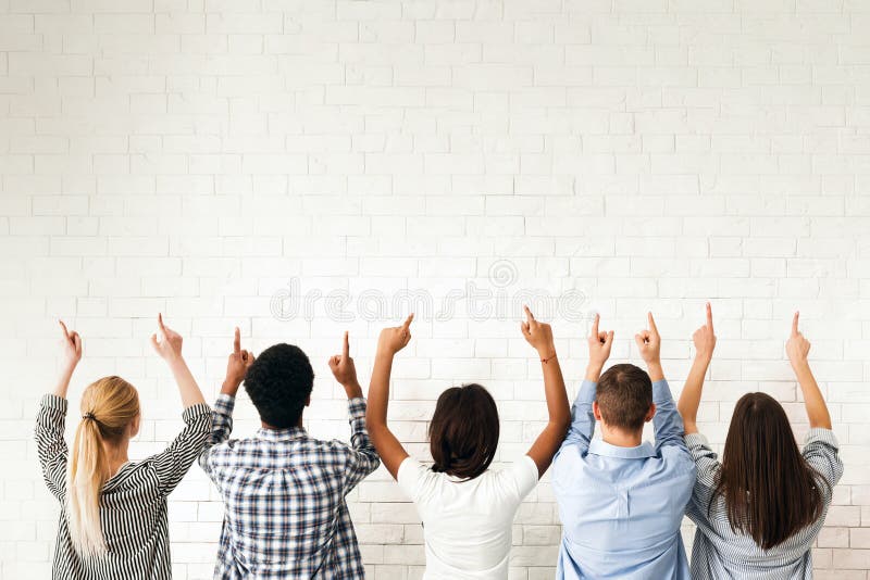 A group of friends stands in front of a blank white wall, all pointing upwards. Their gestures suggest they are indicating or drawing attention to something above them, back view. A group of friends stands in front of a blank white wall, all pointing upwards. Their gestures suggest they are indicating or drawing attention to something above them, back view