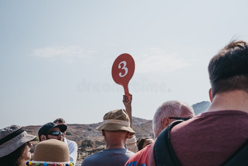 Delos, Greece - September 20, 2019: Tour guide holding group number up on the island of Delos, archaeological site near Mykonos in the Aegean Sea Cyclades archipelago. Selective focus. Delos, Greece - September 20, 2019: Tour guide holding group number up on the island of Delos, archaeological site near Mykonos in the Aegean Sea Cyclades archipelago. Selective focus