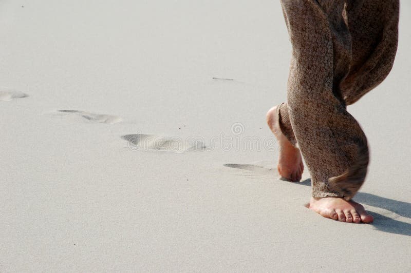 Close-up of legs during a walk. Trousers flapping in the wind. The person has left deep footprints in the sand. Close-up of legs during a walk. Trousers flapping in the wind. The person has left deep footprints in the sand.