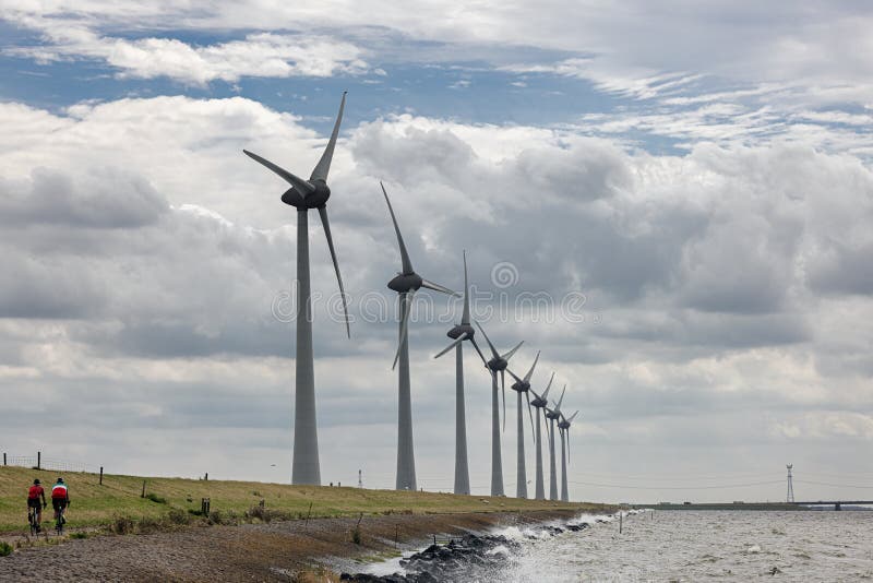 Two lonely Cyclists at Dutch dike IJsselmeer near long row of wind turbines. Two lonely Cyclists at Dutch dike IJsselmeer near long row of wind turbines