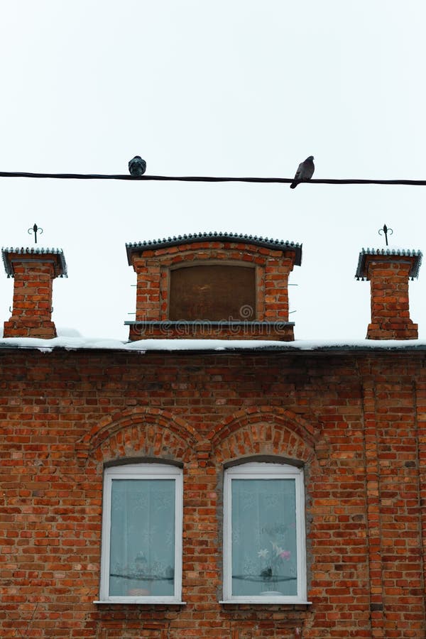 Two pigeons sitting on a wire on top of the frame. An orange brick old building with two (2) windows are in the bottom. Clear sky. Isolated. Two pigeons sitting on a wire on top of the frame. An orange brick old building with two (2) windows are in the bottom. Clear sky. Isolated