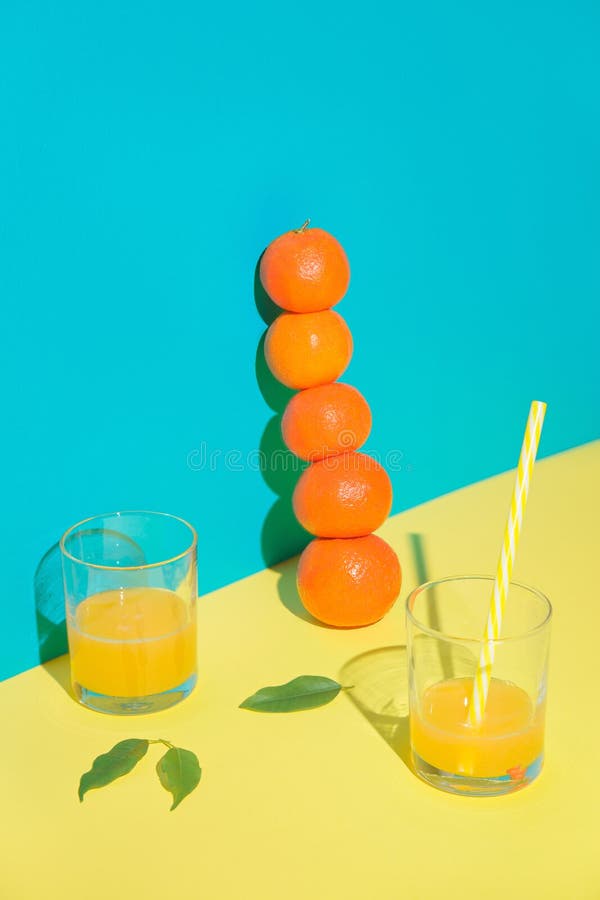 Two cocktail glasses with drinking straws. A vertical pyramid of tangerines. Blue background. Two cocktail glasses with drinking straws. A vertical pyramid of tangerines. Blue background