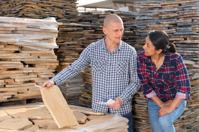 Confident woman shopper discussing with man quality of natural stone tiles at hardware store warehouse. Confident woman shopper discussing with man quality of natural stone tiles at hardware store warehouse