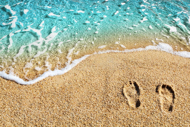 Two footprints on yellow sand, blue sea wave, white foam top view close up, turquoise ocean water, summer vacations on paradise island concept, tropical sunny beach holidays banner, text copy space. Two footprints on yellow sand, blue sea wave, white foam top view close up, turquoise ocean water, summer vacations on paradise island concept, tropical sunny beach holidays banner, text copy space