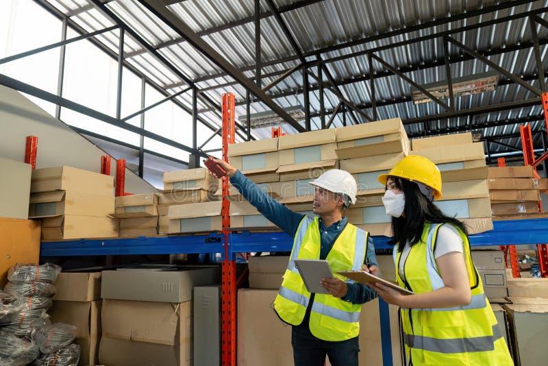 Two smile warehouse workers in uniforms and yellow helmets on heads standing and talking about job. adviser. Two smile warehouse workers in uniforms and yellow helmets on heads standing and talking about job. adviser