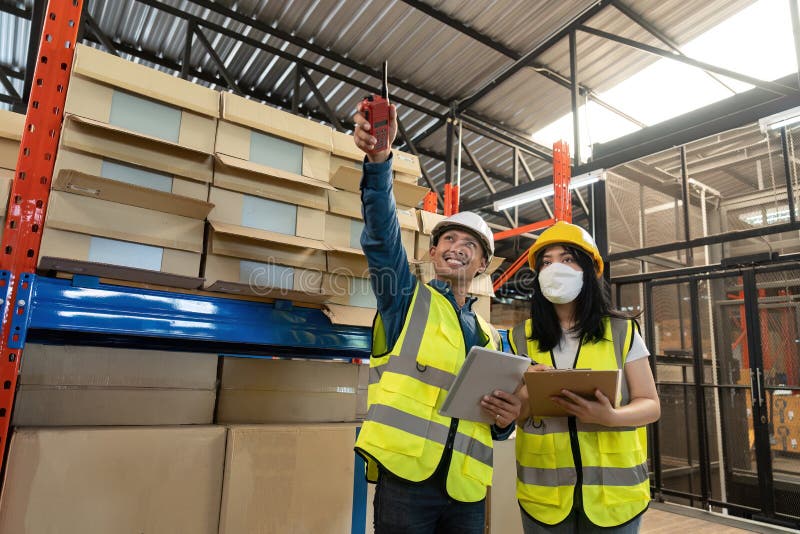 Two smile warehouse workers in uniforms and yellow helmets on heads standing and talking about job. adviser. Two smile warehouse workers in uniforms and yellow helmets on heads standing and talking about job. adviser.