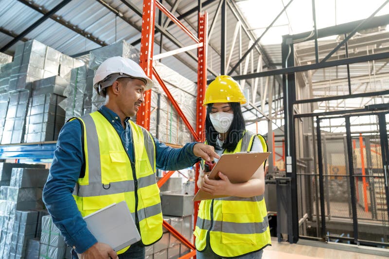 Two smile warehouse workers in uniforms and yellow helmets on heads standing and talking about job. adviser. Two smile warehouse workers in uniforms and yellow helmets on heads standing and talking about job. adviser.