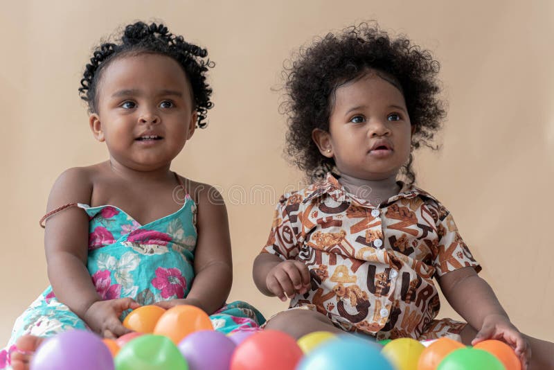 Two Nigerian girls, ages 2 and 1, have beautiful curly hairstyles on a colored background. Sit on the floor with colorful balls. African family concept. Two Nigerian girls, ages 2 and 1, have beautiful curly hairstyles on a colored background. Sit on the floor with colorful balls. African family concept