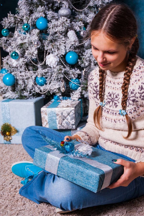 Девочка держа подарок Xmas в руках близко украсила рождественскую елку и камин ели стоковая фотография Девочка держа подарок Xmas в руках близко украсила рождественскую елку и камин ели стоковая фотография
