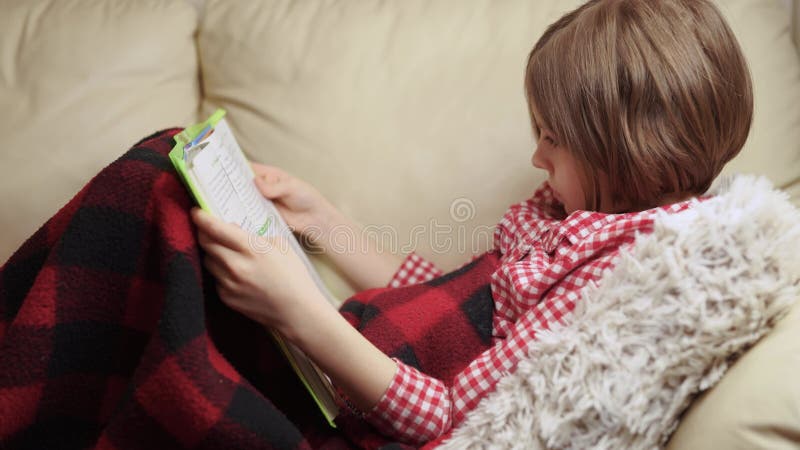 девочка 9 лет читает книгу, лежа на диване. видеоматериал