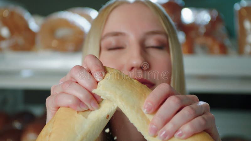 Девочка ломает свежий багет рядом с полок в магазине в пекарне