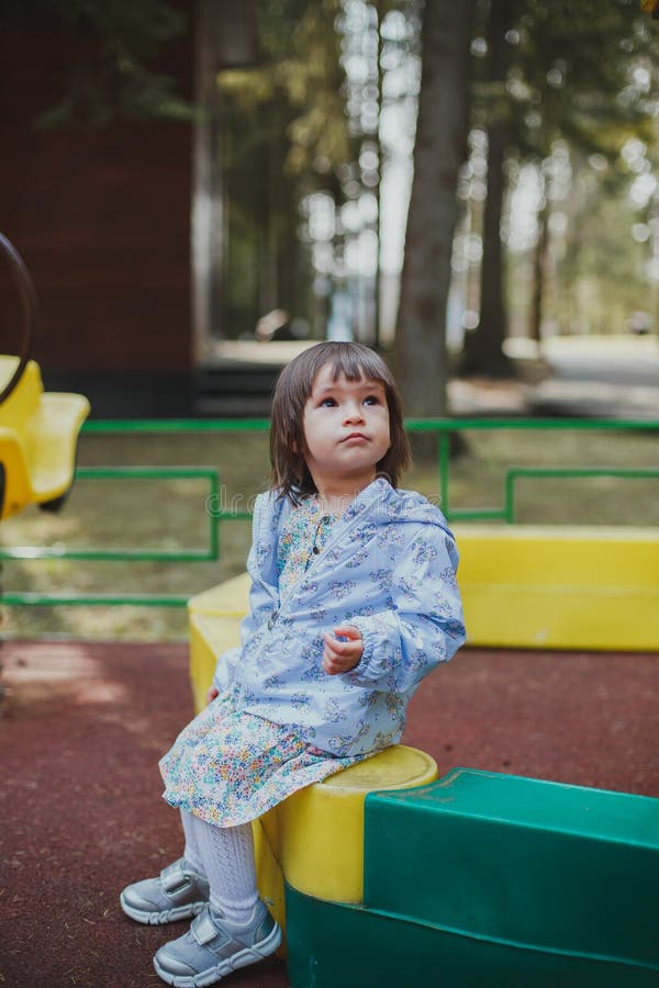 Brunette girl 2 years old in a dress and jacket sitting on the playground. Brunette girl 2 years old in a dress and jacket sitting on the playground