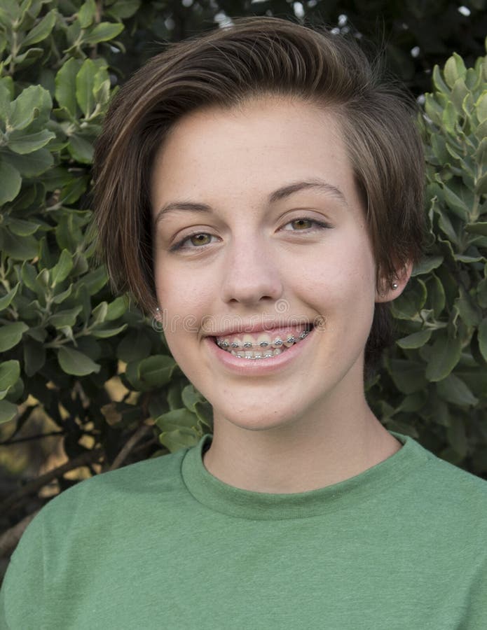 Closeup headshot of a fifteen year old teenage girl. She is smiling and standing in front of a green bush. she has a stylish short haircut and is wearing braces. Closeup headshot of a fifteen year old teenage girl. She is smiling and standing in front of a green bush. she has a stylish short haircut and is wearing braces.