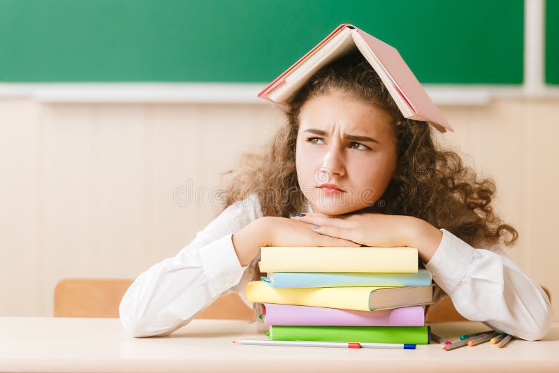 Девушка в школьной форме сидя на ее столе в классе с книгами Студент в ...