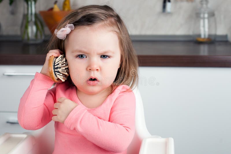 Girl 2 years old playing with a comb at home - portraying an emotional conversation on the phone. Girl 2 years old playing with a comb at home - portraying an emotional conversation on the phone