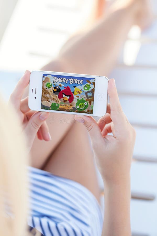 Девушка лежа на салоне фаэтона держа iPhone с игрой сердитым Bir стоковые изображения rf Девушка лежа на салоне фаэтона держа iPhone с игрой сердитым Bir стоковые изображения rf