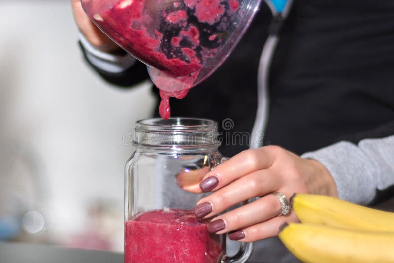 Девушка льет красный smoothie ягоды от blender для того чтобы раздражать стекло стоковое фото rf Девушка льет красный smoothie ягоды от blender для того чтобы раздражать стекло стоковое фото rf