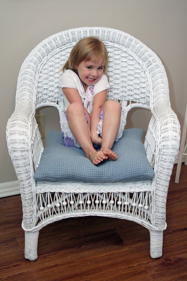 A shy little smiles and sits in a white wicker chair. A shy little smiles and sits in a white wicker chair.