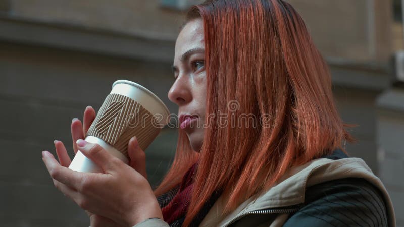Девушка с сексуальными волосами пьет чай в бумажном стакане на улице
