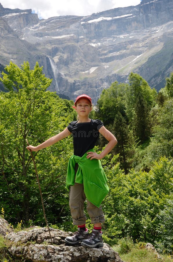 A girl is standing with a crook on the mossy stone. In the background there is a rock amphitheater with the waterfalls of the cirque of Gavarnie in the Pyrenees. A girl is standing with a crook on the mossy stone. In the background there is a rock amphitheater with the waterfalls of the cirque of Gavarnie in the Pyrenees.