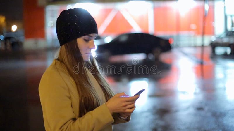Девушка указывая палец на smartphone экрана на свете цвета bokeh освещенности фона в городе ночи атмосферическом сток-видео Девушка указывая палец на smartphone экрана на свете цвета bokeh освещенности фона в городе ночи атмосферическом сток-видео