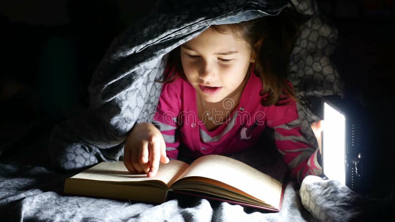 Девушка чтения ребенка предназначенная для подростков читает собаку книги на ноче при электрофонарь лежа под одеялом акции видеоматериалы