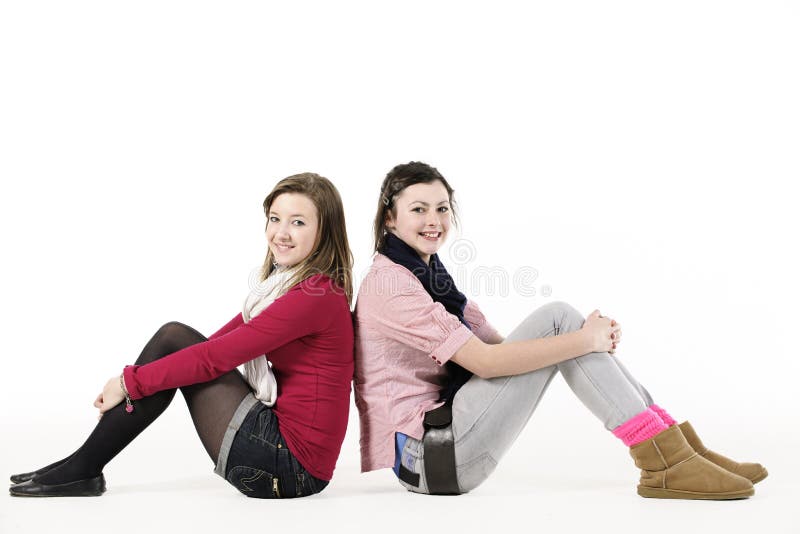 2 teenage girls sitting back to back on white background. 2 teenage girls sitting back to back on white background