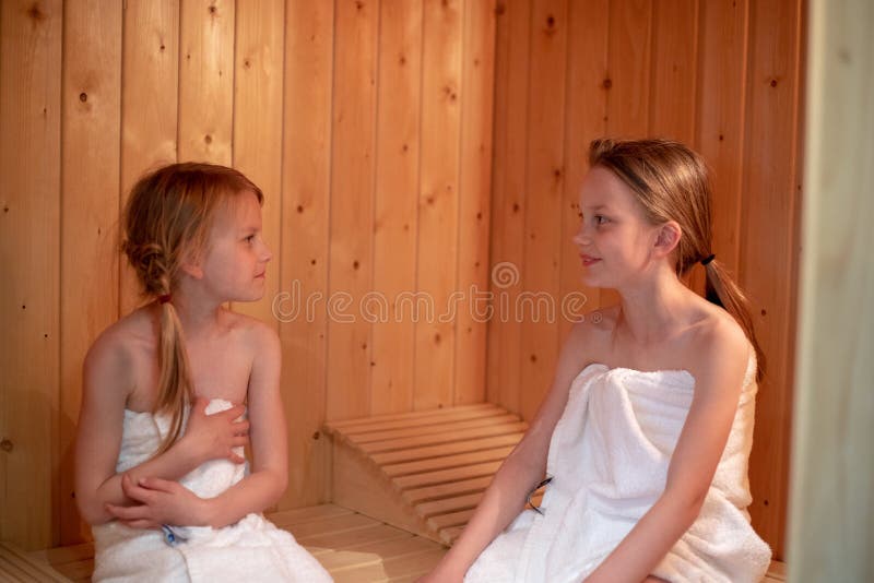Two girls have wrapped themselves in towels and are sitting in a Finnish sauna. Two girls have wrapped themselves in towels and are sitting in a Finnish sauna