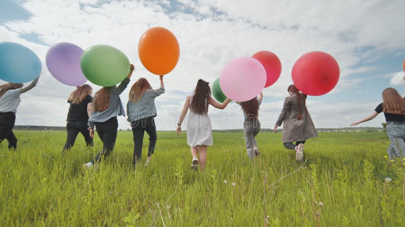 Девушки ходят по полю с большими шариками и красочными шариками.