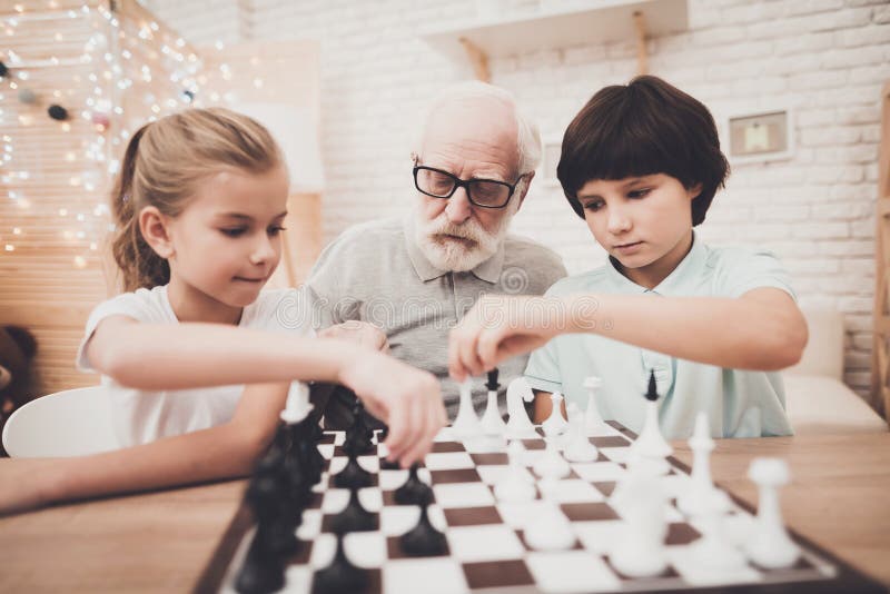 Дед, внук и внучка дома Дети и grandpa играют шахмат стоковое фото rf Дед, внук и внучка дома Дети и grandpa играют шахмат стоковое фото rf