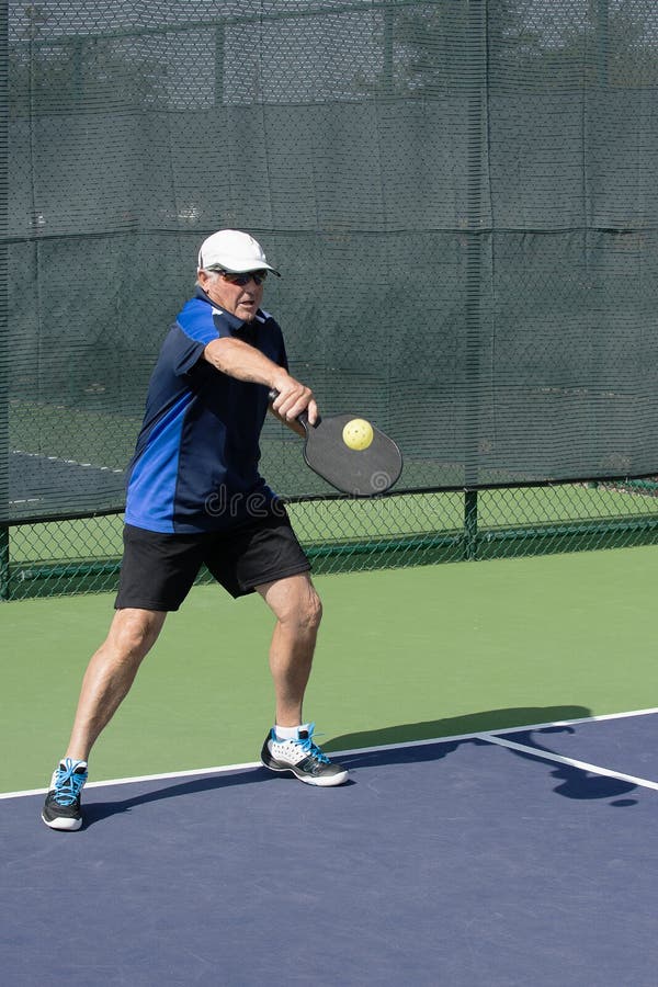 Действие Pickleball - старший человек возвращающ подачу с ходом удара слева стоковое фото rf Действие Pickleball - старший человек возвращающ подачу с ходом удара слева стоковое фото rf