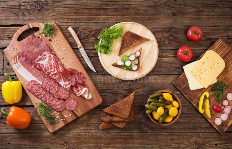 Делая сэндвичи с мясом и колбасой на деревянном столе стоковая фотография