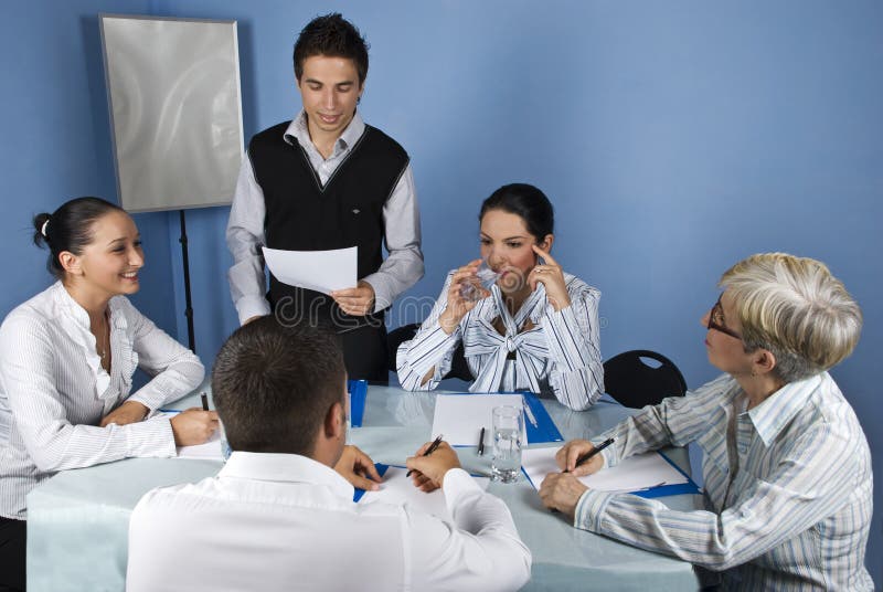 Business meeting with group of people,a businessman making a speech and reading from a paperwork and a businesswoman drinking water and thinking while the others having a conversation,check also. Business meeting with group of people,a businessman making a speech and reading from a paperwork and a businesswoman drinking water and thinking while the others having a conversation,check also