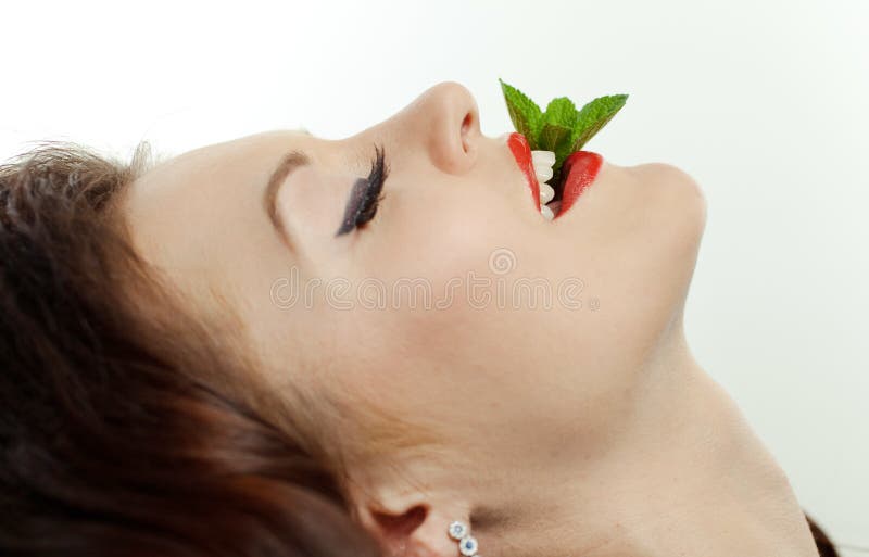 Closeup portrait of a young girl with peppermint by her mouth against white background. Closeup portrait of a young girl with peppermint by her mouth against white background