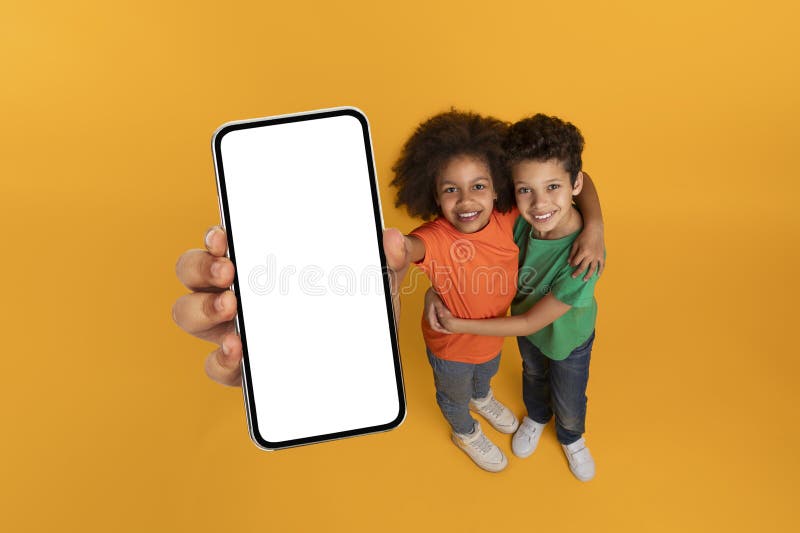 African American kids holding up a cell phone with a blank white screen, showing no content or images, mockup copy space, yellow studio background. African American kids holding up a cell phone with a blank white screen, showing no content or images, mockup copy space, yellow studio background