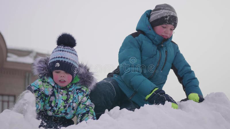 Дети играя на снежной горе, бросая снеге и smejutsja Солнечный морозный день Потеха и игры в свежем воздухе