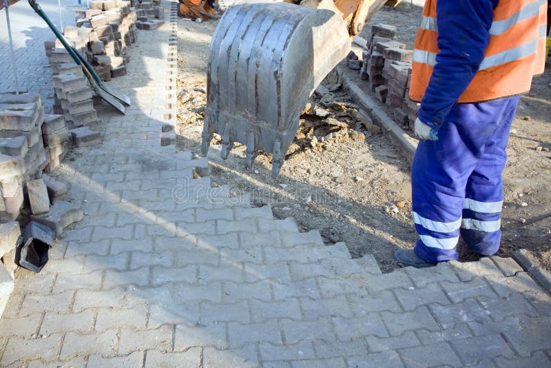 Man repairing sidewalk on construction site. Working with bulldozer scoop. Man repairing sidewalk on construction site. Working with bulldozer scoop.