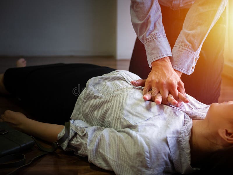 Добровольный ручной насос пользы человека офиса на комоде для CPR скорой помощи аварийного на женщине сердечного приступа обмороч стоковое фото rf Добровольный ручной насос пользы человека офиса на комоде для CPR скорой помощи аварийного на женщине сердечного приступа обмороч стоковое фото rf