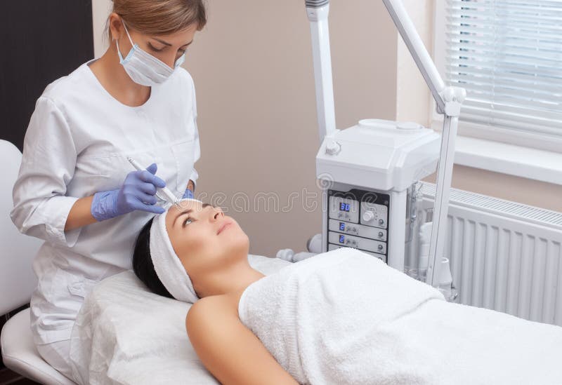 Доктор-cosmetologist делает обработку процедуры Couperose лицевой кожи красивого, молодой женщины стоковое фото rf Доктор-cosmetologist делает обработку процедуры Couperose лицевой кожи красивого, молодой женщины стоковое фото rf