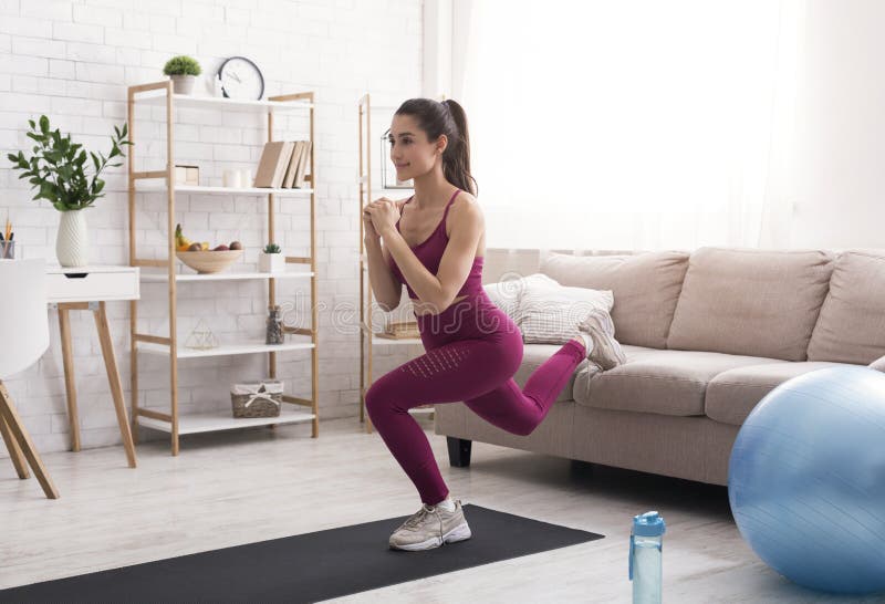 At home workout routine. Lovely Latin girl training indoors, doing lunges near sofa. At home workout routine. Lovely Latin girl training indoors, doing lunges near sofa