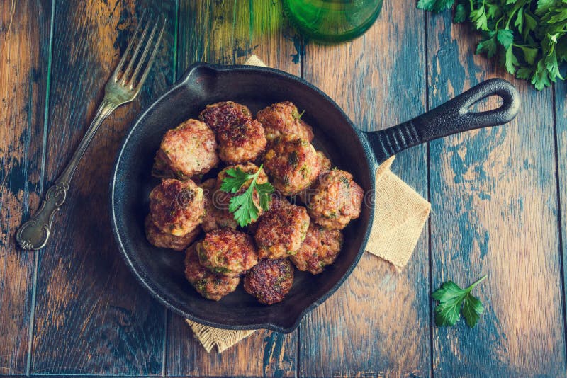 Домодельные зажаренные в духовке фрикадельки говядины в skillet чугуна на деревянном столе в кухне, свежей петрушке, винтажной ви стоковые изображения Домодельные зажаренные в духовке фрикадельки говядины в skillet чугуна на деревянном столе в кухне, свежей петрушке, винтажной ви стоковые изображения