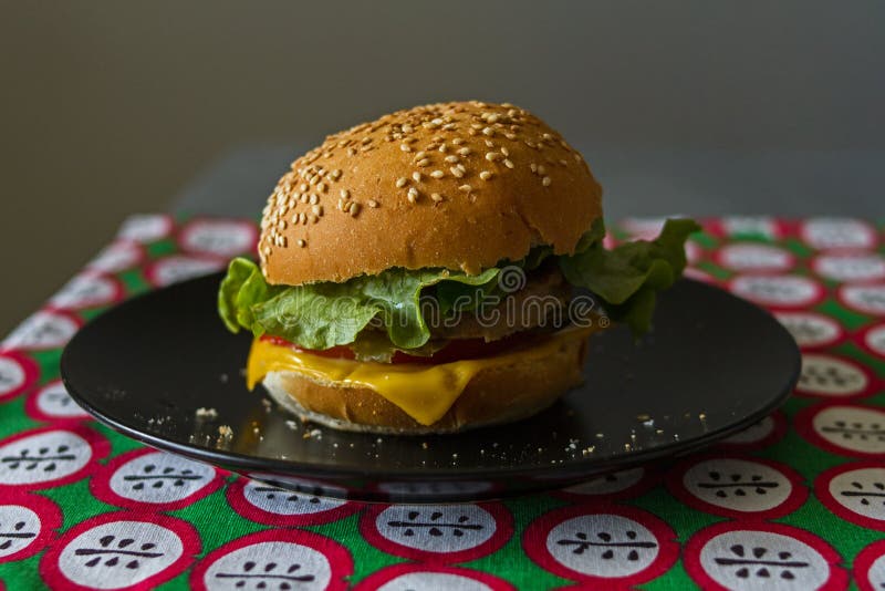 Домодельный аппетитный cheeseburger с расплавленным сыром в провозглашанной тост плюшке с сезамом на красной скатерти на серой пр стоковая фотография Домодельный аппетитный cheeseburger с расплавленным сыром в провозглашанной тост плюшке с сезамом на красной скатерти на серой пр стоковая фотография