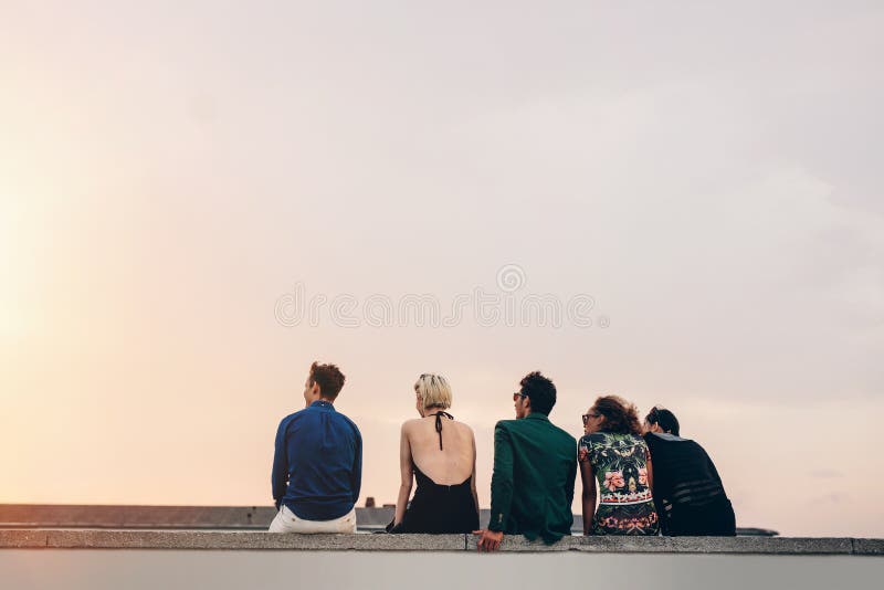 Друзья сидя совместно на крыше на заходе солнца