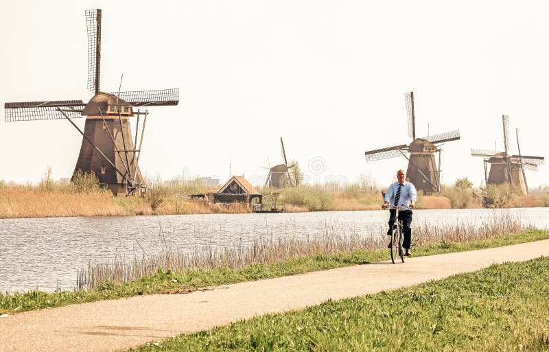 Kinderdijk, Netherlands - April 1, 2014: Dutchman on a bicycle with  famous windmills in Kinderdijk at background. Kinderdijk, Netherlands - April 1, 2014: Dutchman on a bicycle with  famous windmills in Kinderdijk at background.