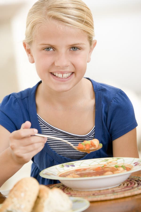 Young girl indoors eating soup smiling. Young girl indoors eating soup smiling