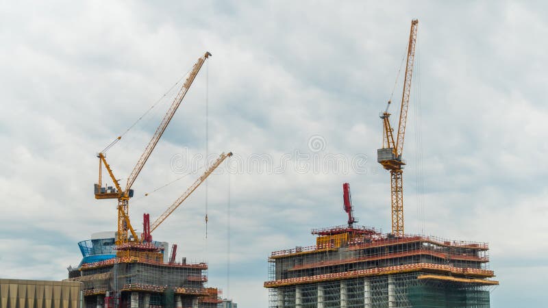 Yellow tower cranes and unfinished building construction against dramatic cloudy grey sky. Building process, urban, engineering, city developing industrial concept. Yellow tower cranes and unfinished building construction against dramatic cloudy grey sky. Building process, urban, engineering, city developing industrial concept
