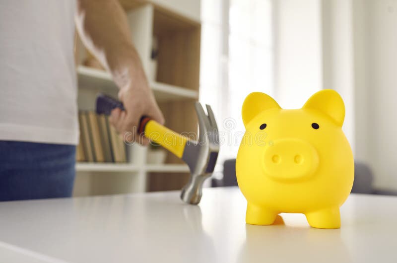 Cute yellow ceramic piggy bank about to be smashed with a hammer. Man in dire need of money is going to break his piggybank on the table. Cropped close up shot. Saving up, or being in debt concepts. Cute yellow ceramic piggy bank about to be smashed with a hammer. Man in dire need of money is going to break his piggybank on the table. Cropped close up shot. Saving up, or being in debt concepts