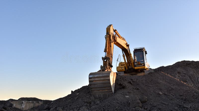 Желтый экскаватор во время earthmoving на открытом карьере на фоне голубого неба.. Строительная техника и earthmoving тяжелое обор стоковая фотография