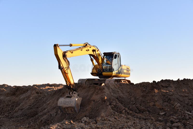 Желтый экскаватор во время earthmoving на открытом карьере на фоне голубого неба.. Строительная техника и earthmoving тяжелое обор стоковое изображение rf