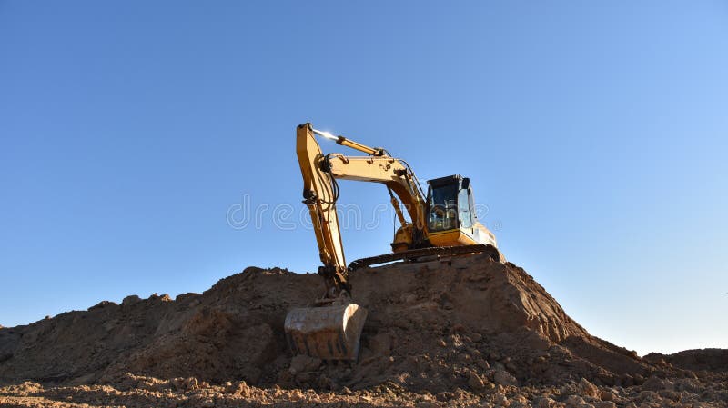 Желтый экскаватор во время earthmoving на открытом карьере на фоне голубого неба.. Строительная техника и earthmoving тяжелое обор стоковые фотографии rf
